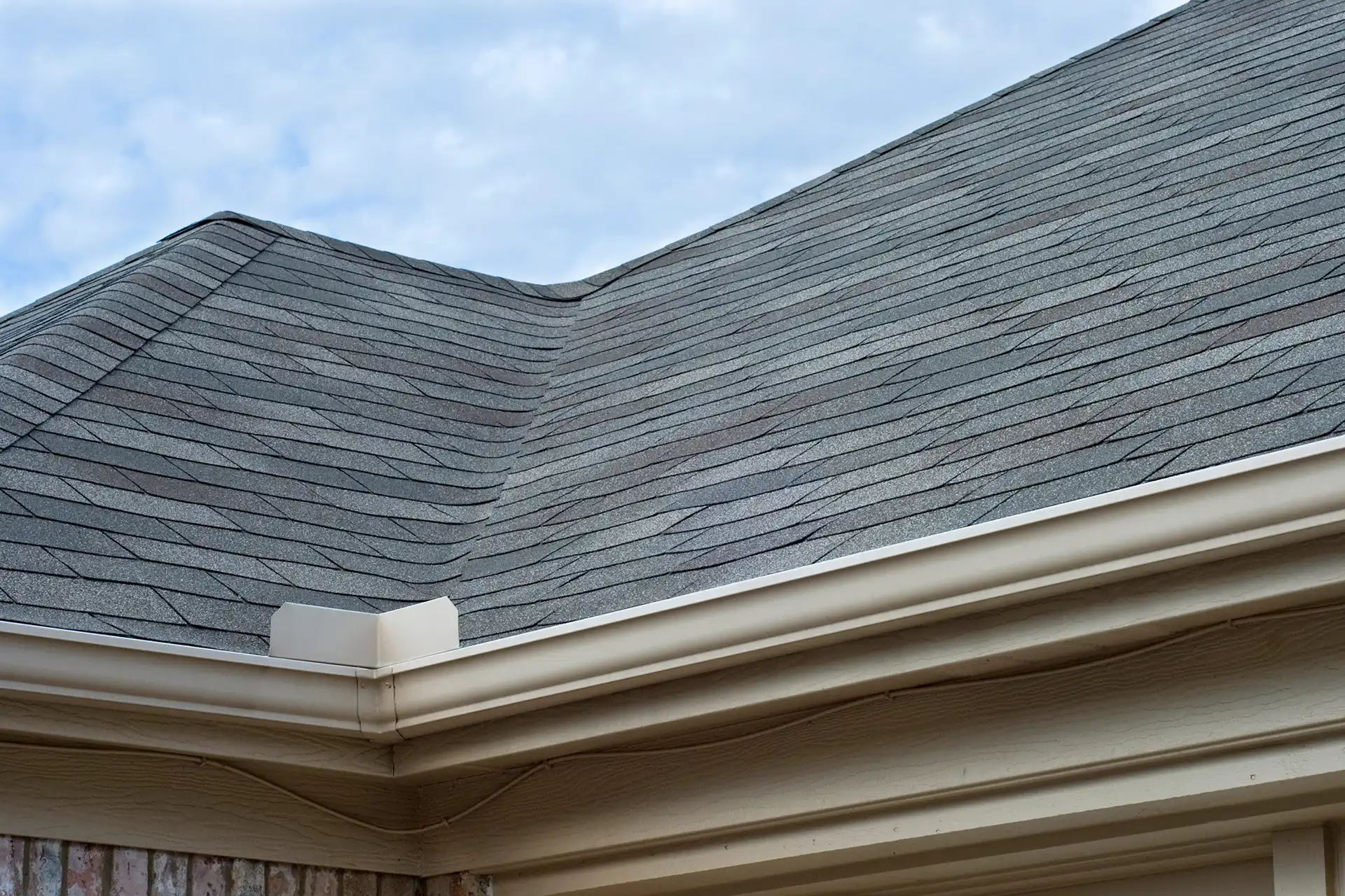 A clean beige gutter system installed along the roofline of a house with gray shingles