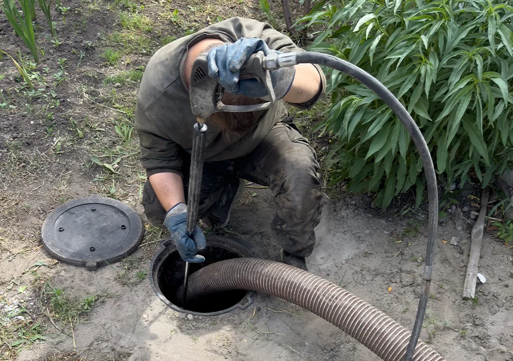 A technician using a high-pressure hose and vacuum line to clean or clear an underground septic or sewer tank