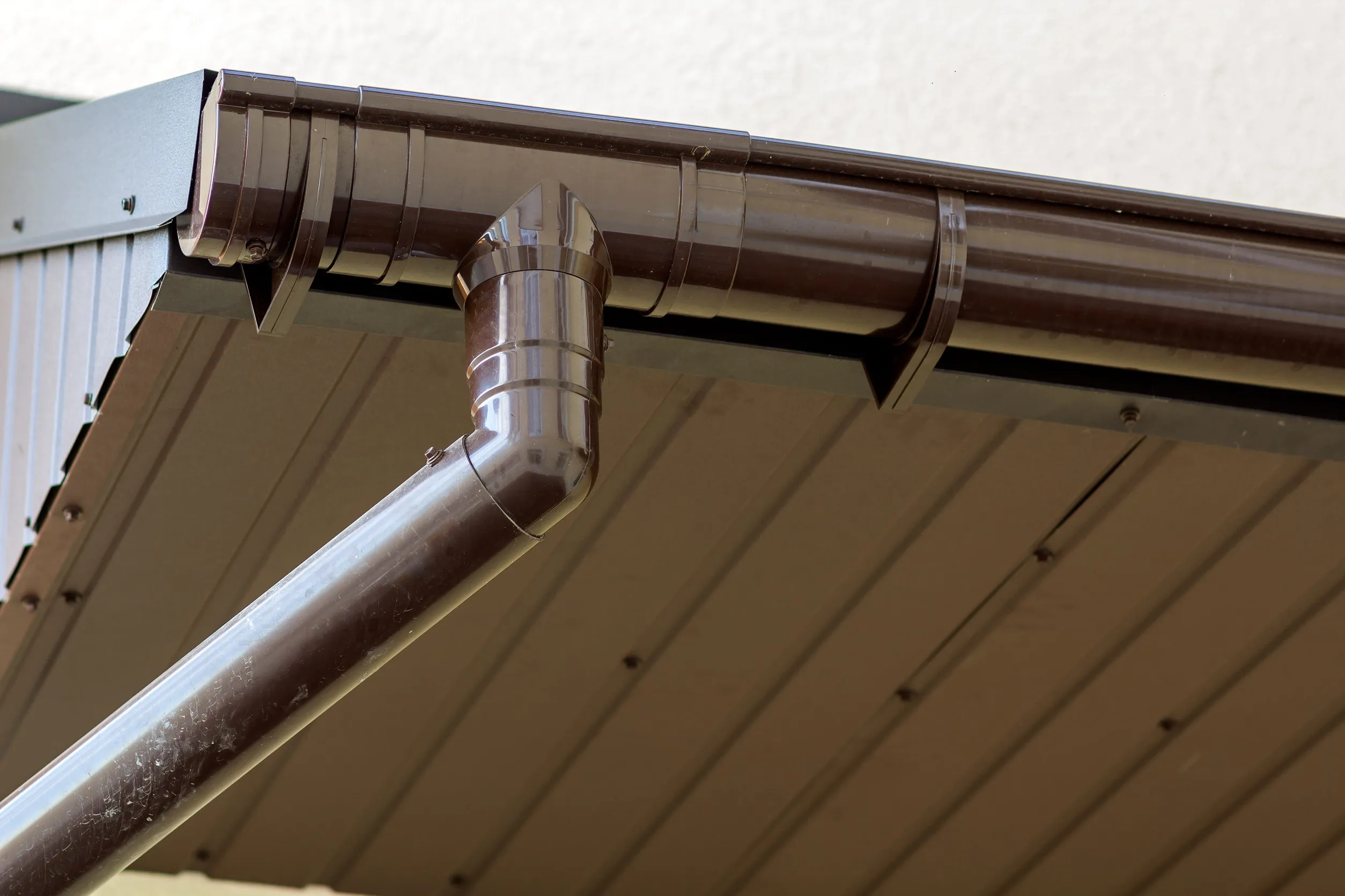 Close-up detail of cottage house corner with brown metal planks siding and roof with steel gutter rain system