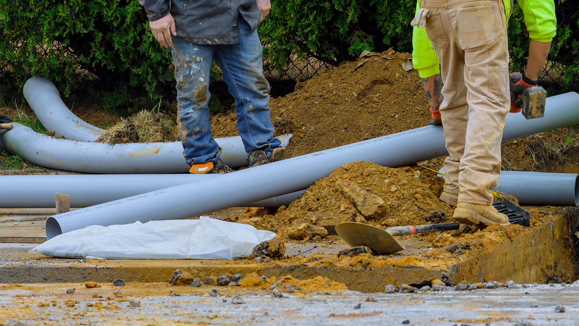 Construction workers moving large grey PVC utility pipes at an excavation site