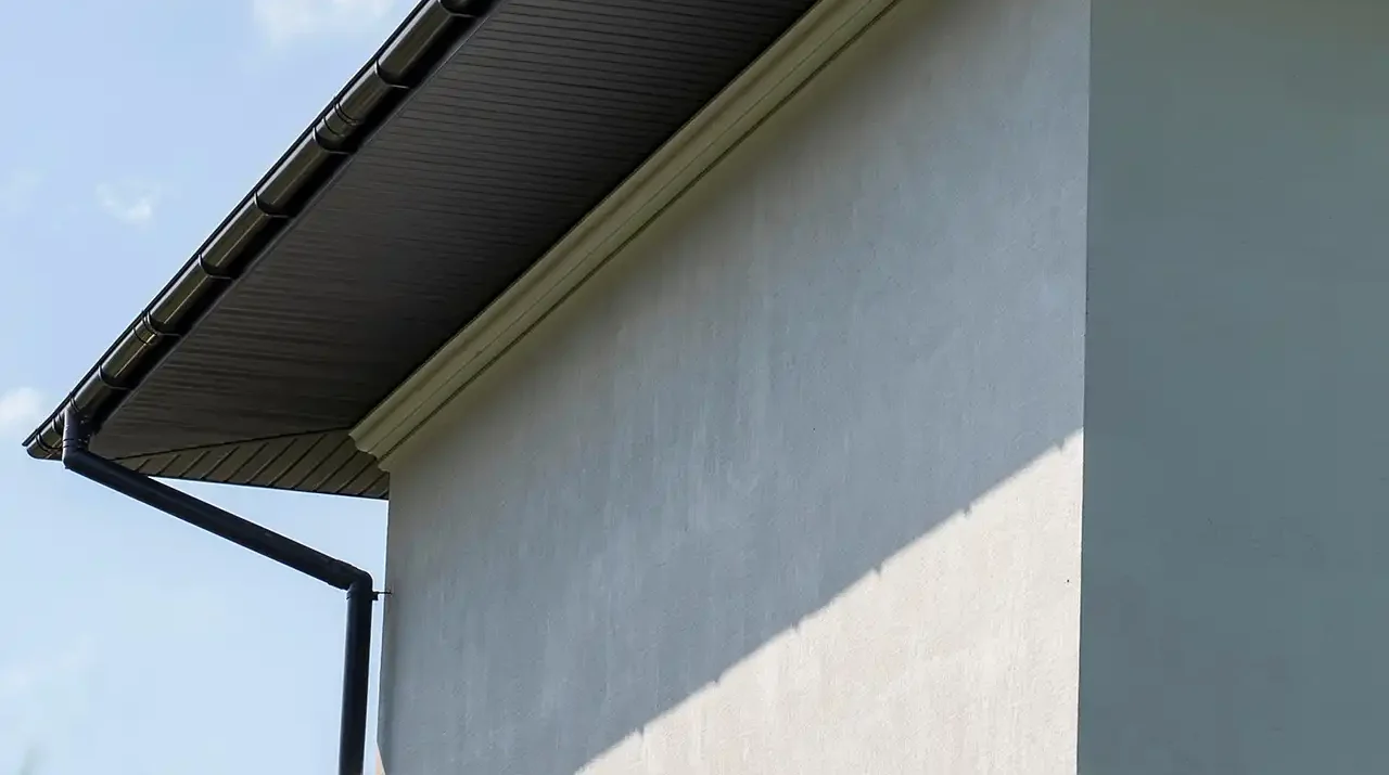 Low-angle view of a dark-colored vented soffit and gutter system on a white exterior wall