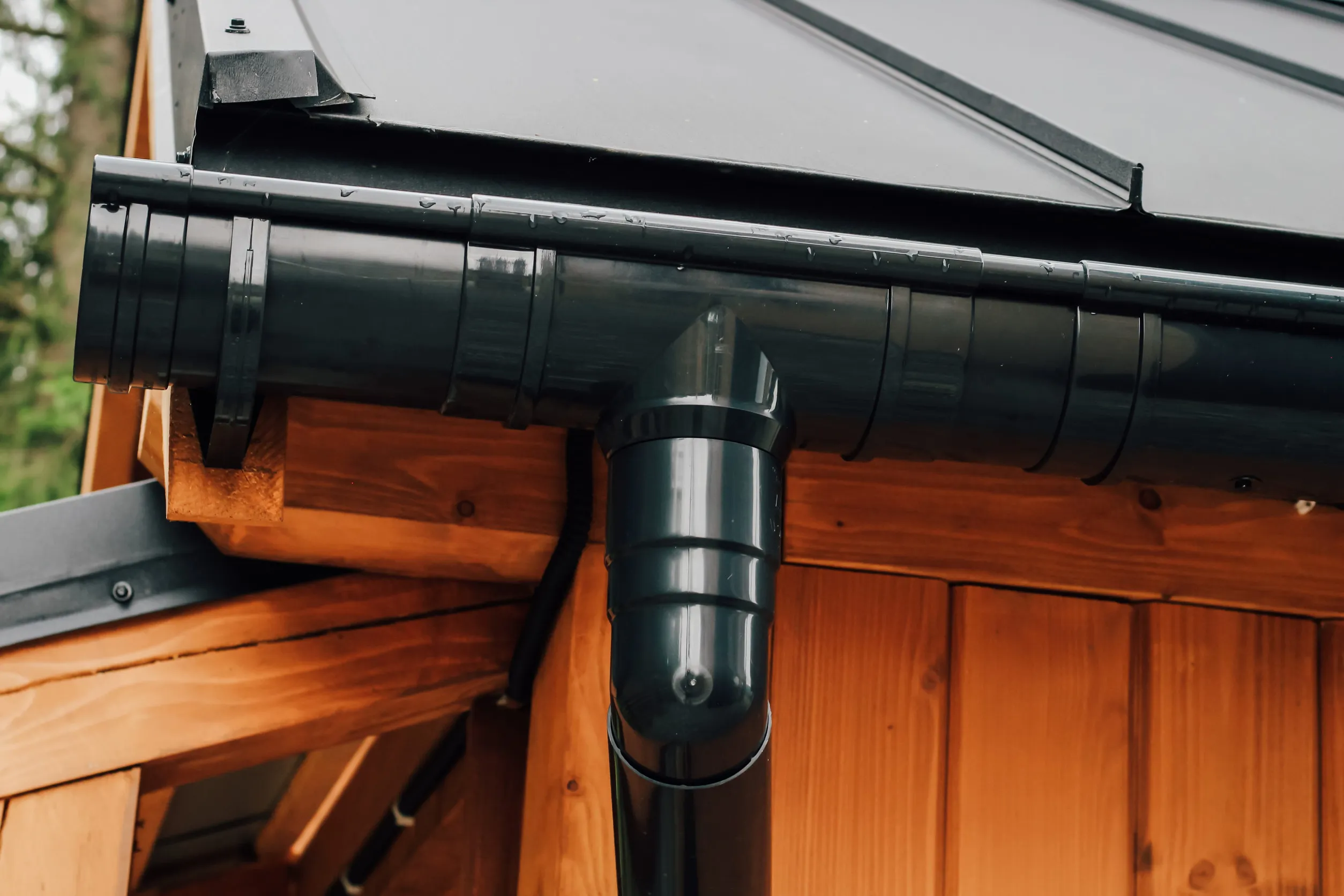 Water drainage system features a black gutter attached to a wooden cabin roof