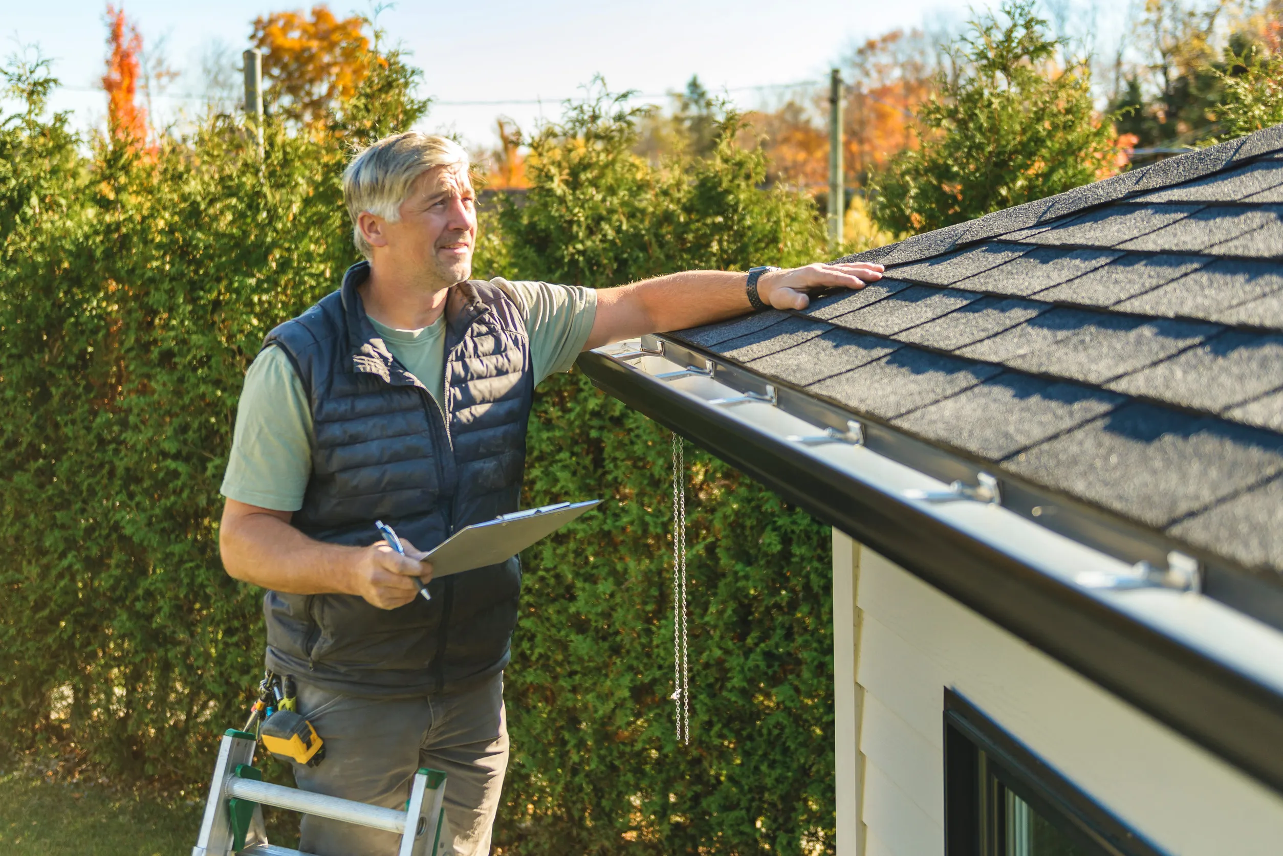 man standing on steps inspecting house roof