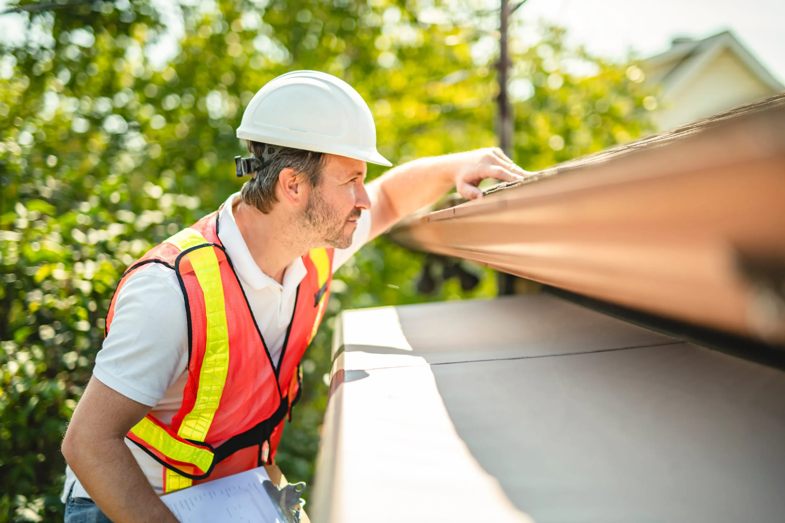man with hard hat standing on steps inspecting house roof